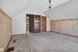 Sloped ceilings defining an expansive room with carpet flooring, a dark wood-finish door, and additional louvered closet doors - 