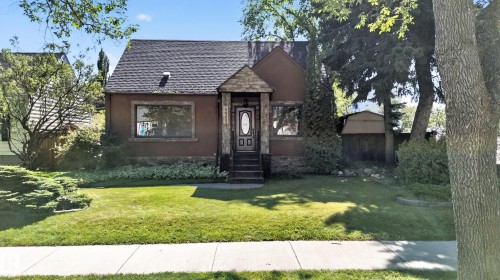 Stucco exterior with stone detailing, covered entry, front lawn with established landscaping, and mature trees - 13351 109A Avenue Nw, Edmonton, AB 