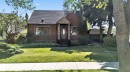 Stucco exterior with stone detailing, covered entry, front lawn with established landscaping, and mature trees - 13351 109A Avenue Nw, Edmonton, AB 