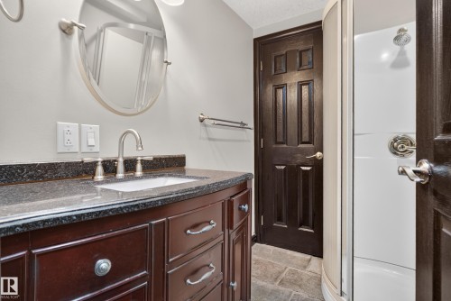 Cherry wood-finish vanity with a dark speckled countertop, undermount sink, and brushed nickel faucet - 13351 109A Avenue Nw, Edmonton, AB 