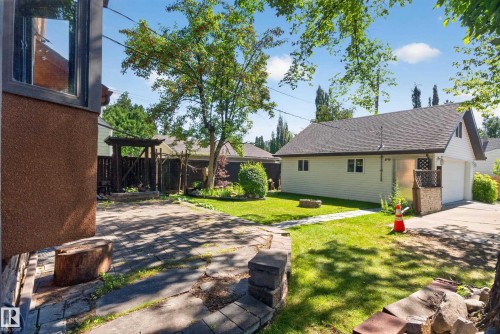 Spacious backyard with a detached garage, mature trees, a paved patio area, and a green lawn - 13351 109A Avenue Nw, Edmonton, AB 