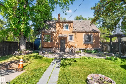 Stucco exterior with stone accents, bay window, front patio area, stone pathway, and mature trees - 13351 109A Avenue Nw, Edmonton, AB 
