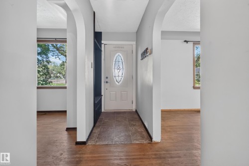 Arched doorways frame the entry, featuring a front door with an oval stained-glass insert, tile flooring, and a built-in storage unit - 13351 109A Avenue Nw, Edmonton, AB 