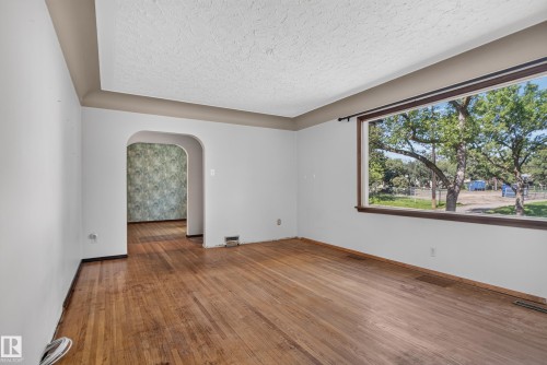Expansive window with dark trim, wood-finish flooring, light-toned walls, and an arched doorway - 13351 109A Avenue Nw, Edmonton, AB 