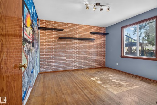 Brick accent wall with floating shelves, wood-finish flooring, and a large window with wood trim - 13351 109A Avenue Nw, Edmonton, AB 