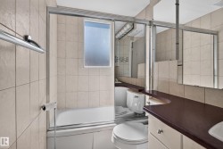 Floor-to-ceiling tiled walls, enclosed bathtub with sliding glass doors, horizontal transom window, extended vanity with integrated sink, and overhead multi-bulb lighting fixture - 