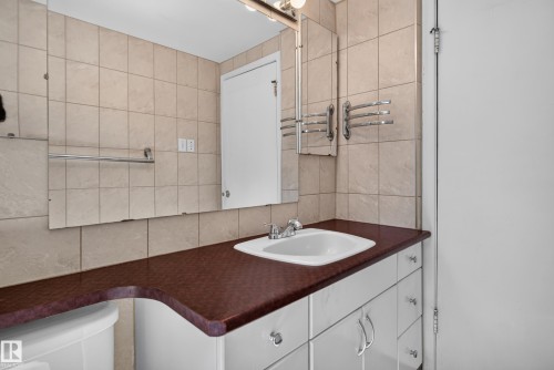 Bathroom featuring a curved wood-finish vanity countertop with an integrated white basin sink, white cabinetry with chrome hardware, and ceramic tile wall surfaces - 13351 109A Avenue Nw, Edmonton, AB 
