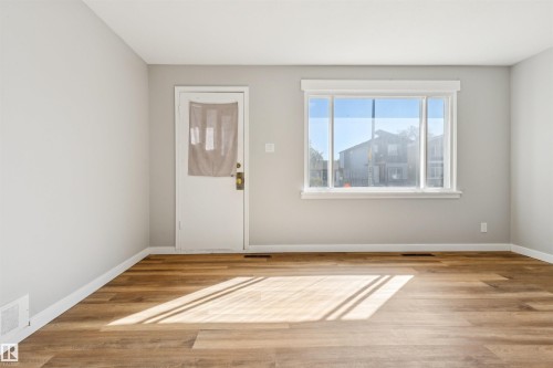Wood-finish flooring, light gray wall paint, and a white entry door with brass hardware - 10916 151 Street Nw, Edmonton, AB 