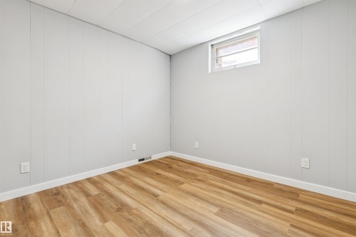 Room featuring wood-finish flooring, light-toned wall paneling, a drop ceiling, and a single window - 10916 151 Street Nw, Edmonton, AB 