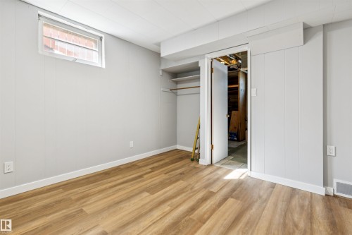 Wood-finish flooring, white wall paneling, white trim, drop ceiling, and a built-in closet with shelving and hanging rod - 10916 151 Street Nw, Edmonton, AB 