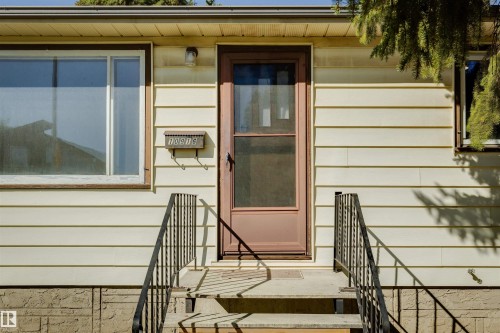 Siding exterior with a storm door, concrete steps, and black metal handrails - 10916 151 Street Nw, Edmonton, AB 