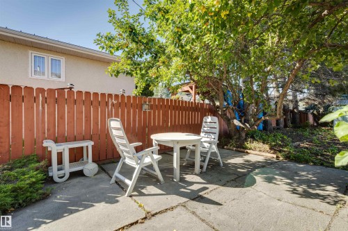 Picket fence with decorative post caps, concrete patio, mature tree, and planted greenery - 10916 151 Street Nw, Edmonton, AB 