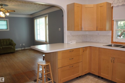 Functional kitchen with wood-finish cabinetry, light-toned countertops, and dual stainless steel sink - 4406 49A Street, Vegreville, AB 