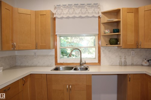 Kitchen featuring wood-finish cabinetry, solid surface countertops, a double basin stainless steel sink, and a tiled backsplash - 4406 49A Street, Vegreville, AB 