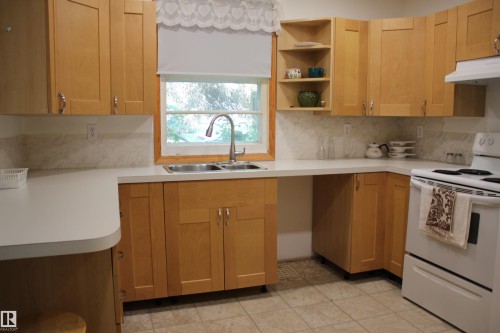 Light wood-finish cabinetry with silver-tone hardware, white countertops, tile backsplash, and a double basin stainless steel sink with a gooseneck faucet - 4406 49A Street, Vegreville, AB 