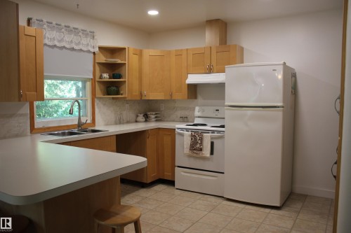Warm wood cabinetry and stainless steel appliances define this kitchen, featuring ample counter space, a large refrigerator, and built-in stovetop with oven - 4406 49A Street, Vegreville, AB 