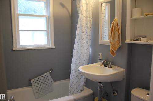 Built-in shelving, corner sink, white framed window, wall-mounted mirror, and a white bathtub - 4406 49A Street, Vegreville, AB 