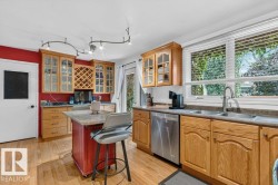 Kitchen featuring wood-finish flooring, wood cabinetry with glass-front uppers and integrated wine storage, a central island with a stone-finish countertop, and a double basin stainless steel sink with a gooseneck faucet - 