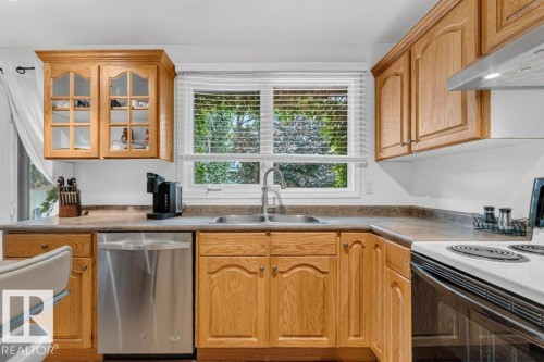 Kitchen featuring wood cabinetry, stainless steel dishwasher, double basin sink, and laminate countertops - 11131 35A Avenue Nw, Edmonton, AB - Indoor Photo Showing Kitchen With Double Sink