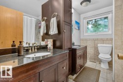 Bathroom featuring dark wood-finish cabinetry, a dual-sink vanity with dark countertops, tiled flooring, and a window with a privacy screen - 