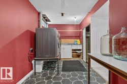 Dedicated laundry area featuring a patterned stone-look flooring, white base cabinetry with shelving, and a wood-finish countertop - 