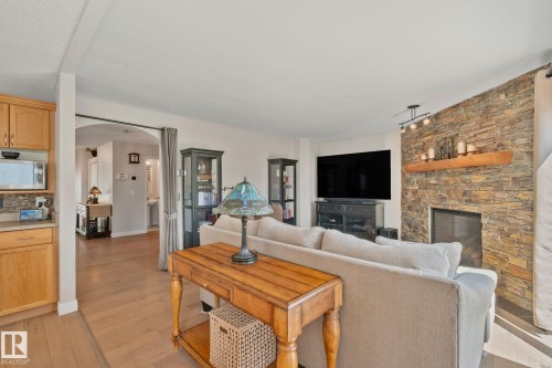 Living area featuring a stone accent wall, fireplace with a wood mantel, and wood-finish flooring - 591 Byrne Crescent Sw, Edmonton, AB 