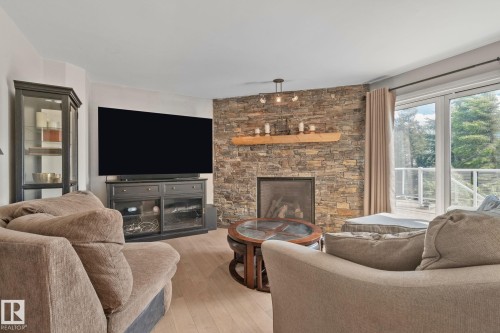 Stone-clad fireplace with a wood mantel, light wood-finish flooring, recessed lighting, and sliding glass doors - 591 Byrne Crescent Sw, Edmonton, AB 