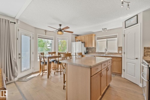 Kitchen featuring a central island, wood-finish flooring, light wood cabinetry, and a textured tile backsplash - 591 Byrne Crescent Sw, Edmonton, AB 