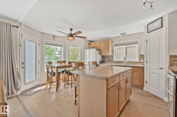 Kitchen featuring a central island, wood-finish flooring, light wood cabinetry, and a textured tile backsplash - 
