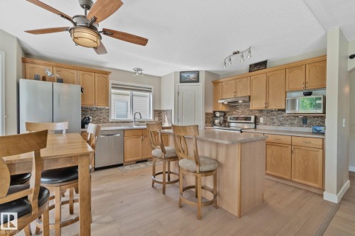 Kitchen featuring light wood cabinetry, stainless steel appliances, a center island with bar seating, and wood-finish flooring - 591 Byrne Crescent Sw, Edmonton, AB 