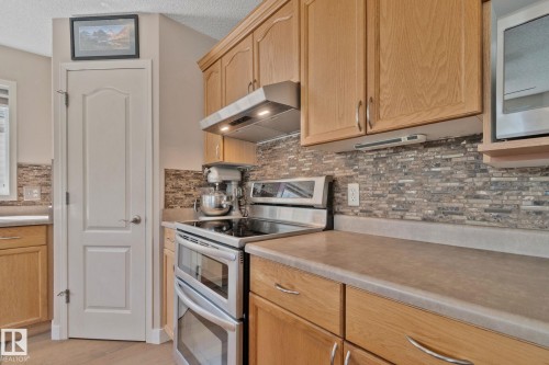 Wood-finish cabinetry paired with a mosaic tile backsplash, featuring stainless steel appliances including a double oven range and built-in microwave - 591 Byrne Crescent Sw, Edmonton, AB 