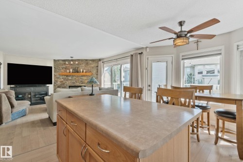 Kitchen island with integrated storage, wood-finish flooring, stone-clad fireplace, sliding glass door, and ceiling fan with integrated lighting - 591 Byrne Crescent Sw, Edmonton, AB 