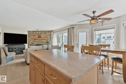 Kitchen island with integrated storage, wood-finish flooring, stone-clad fireplace, sliding glass door, and ceiling fan with integrated lighting - 
