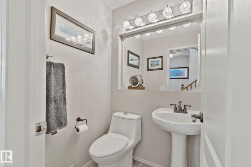 Pedestal sink with a two-handle faucet, wall-mounted mirror, and vanity lighting fixture - 591 Byrne Crescent Sw, Edmonton, AB 