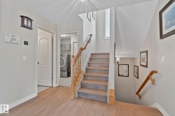 Hardwood flooring with a natural finish, wooden staircase with matching banister, integrated laundry area with washer and dryer, ceiling-mounted light fixture, and wall-mounted sconce lighting - 