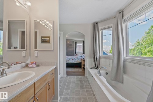 Tiled flooring with a built-in bathtub, dual windows, and a vanity with an integrated sink and wood-finish cabinetry - 591 Byrne Crescent Sw, Edmonton, AB 