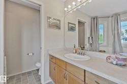 Wood-finish vanity with a light-toned countertop, undermount sink, and wall-mounted mirror with overhead lighting - 