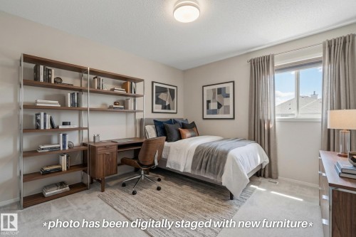 Light-colored wall paint and carpeting, large window with ample natural light, built-in desk with shelving, and a flush-mount ceiling light - 591 Byrne Crescent Sw, Edmonton, AB 