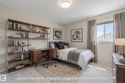 Light-colored wall paint and carpeting, large window with ample natural light, built-in desk with shelving, and a flush-mount ceiling light - 