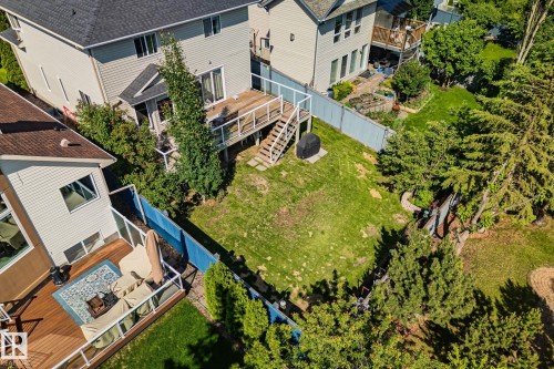 Expansive backyard featuring a large wooden deck with glass panel railing, a separate ground-level patio, and mature trees - 591 Byrne Crescent Sw, Edmonton, AB 