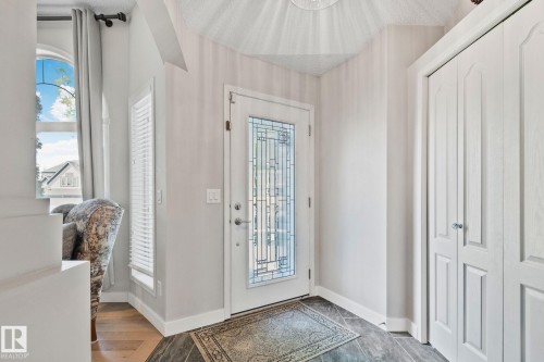 Entryway featuring a decorative glass front door, bifold closet doors, and mixed flooring with wood-finish and tile - 591 Byrne Crescent Sw, Edmonton, AB 