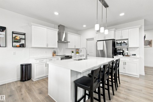 White shaker cabinetry, stainless steel appliances, white subway tile backsplash, white countertop island, wood-finish flooring - 107 Ellice Bend, Fort Saskatchewan, AB 