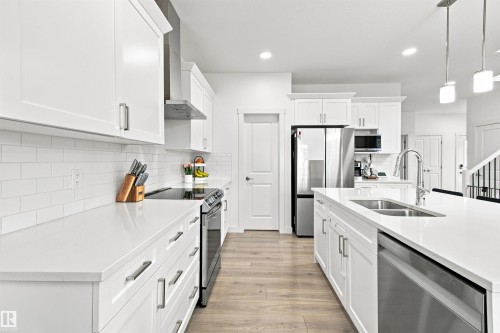 Modern kitchen featuring white cabinetry, light countertops, wood-finish flooring, stainless steel appliances, and a central island with an undermount sink - 107 Ellice Bend, Fort Saskatchewan, AB 