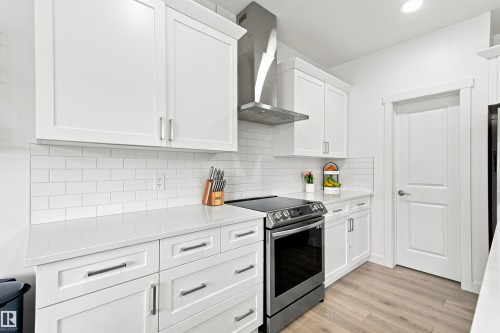 White shaker cabinetry with brushed nickel hardware, light-toned countertops, subway tile backsplash, stainless steel range with hood, and wood-finish flooring - 107 Ellice Bend, Fort Saskatchewan, AB 