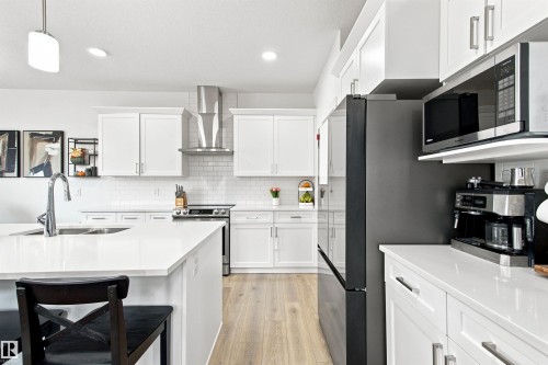 Spacious kitchen featuring white cabinetry, light wood-finish flooring, stainless steel appliances, white subway tile backsplash, and a large island with an undermount sink - 107 Ellice Bend, Fort Saskatchewan, AB 