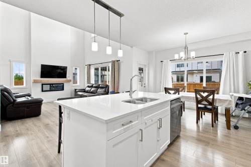 Open-concept living area featuring a kitchen island with dual sinks, white cabinetry, and stainless steel appliances - 107 Ellice Bend, Fort Saskatchewan, AB 
