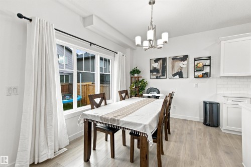 Expansive window with white trim, wood-finish flooring, white cabinetry, subway tile backsplash, and a modern chandelier - 107 Ellice Bend, Fort Saskatchewan, AB 