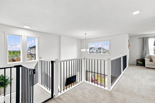 Second-story landing with recessed lighting, light-colored carpeting, white balusters, and black metal spindles - 107 Ellice Bend, Fort Saskatchewan, AB 