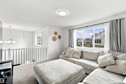 Carpeted living area with a large multi-pane window, white walls, and a flush-mount ceiling light - 107 Ellice Bend, Fort Saskatchewan, AB 