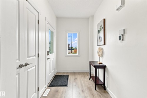 Bright entryway showcasing wood-finish flooring, white shaker-style cabinetry, and abundant natural light from a centered entry door - 107 Ellice Bend, Fort Saskatchewan, AB 